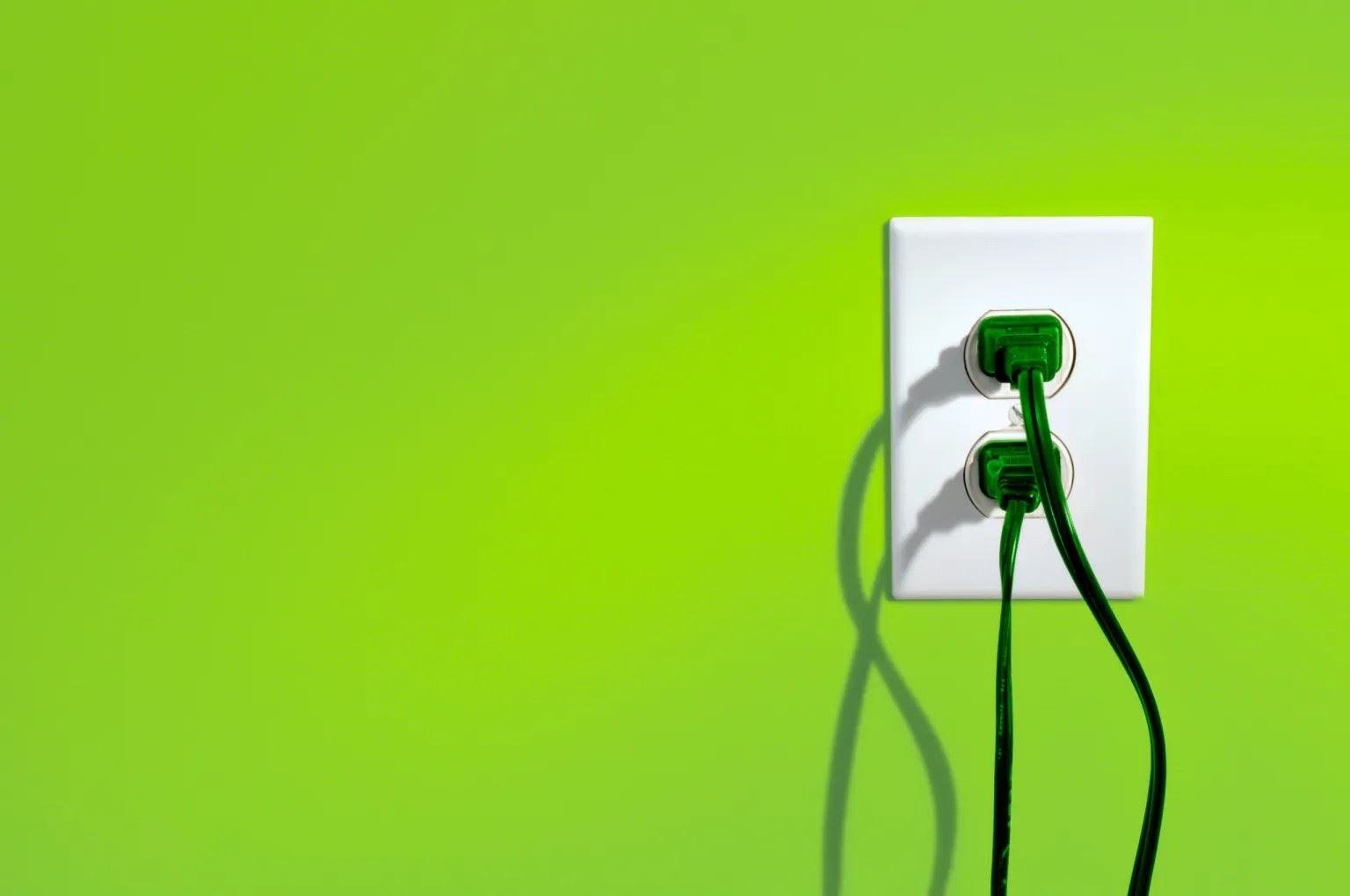 An outlet in a vibrant green wall with dark green plugs plugged in 