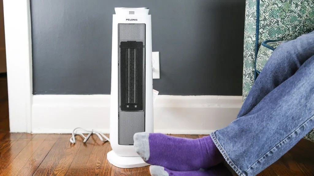 Portable space heater plugged into a wall outlet near a person’s feet, highlighting home heating and electrical safety.