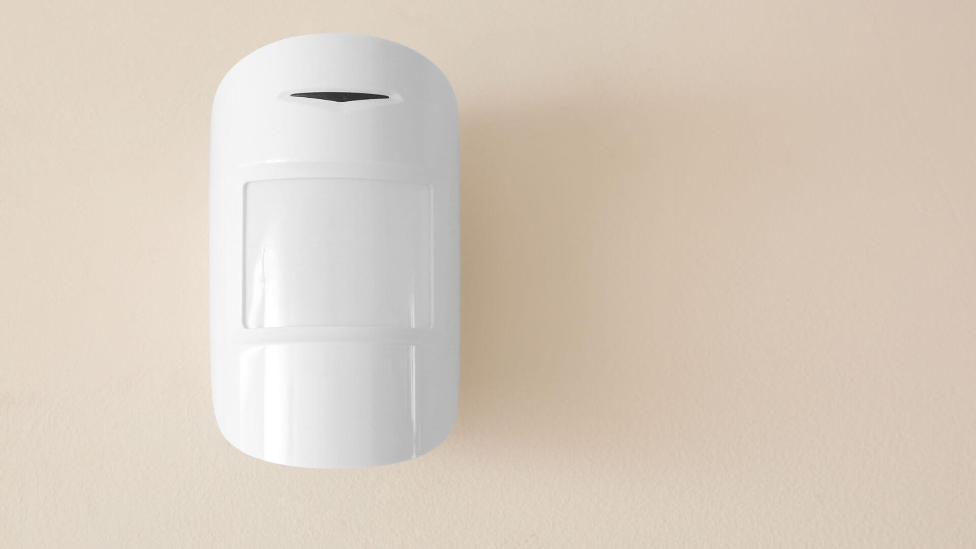 White motion sensor mounted on a beige wall, used for home security and automated lighting systems.